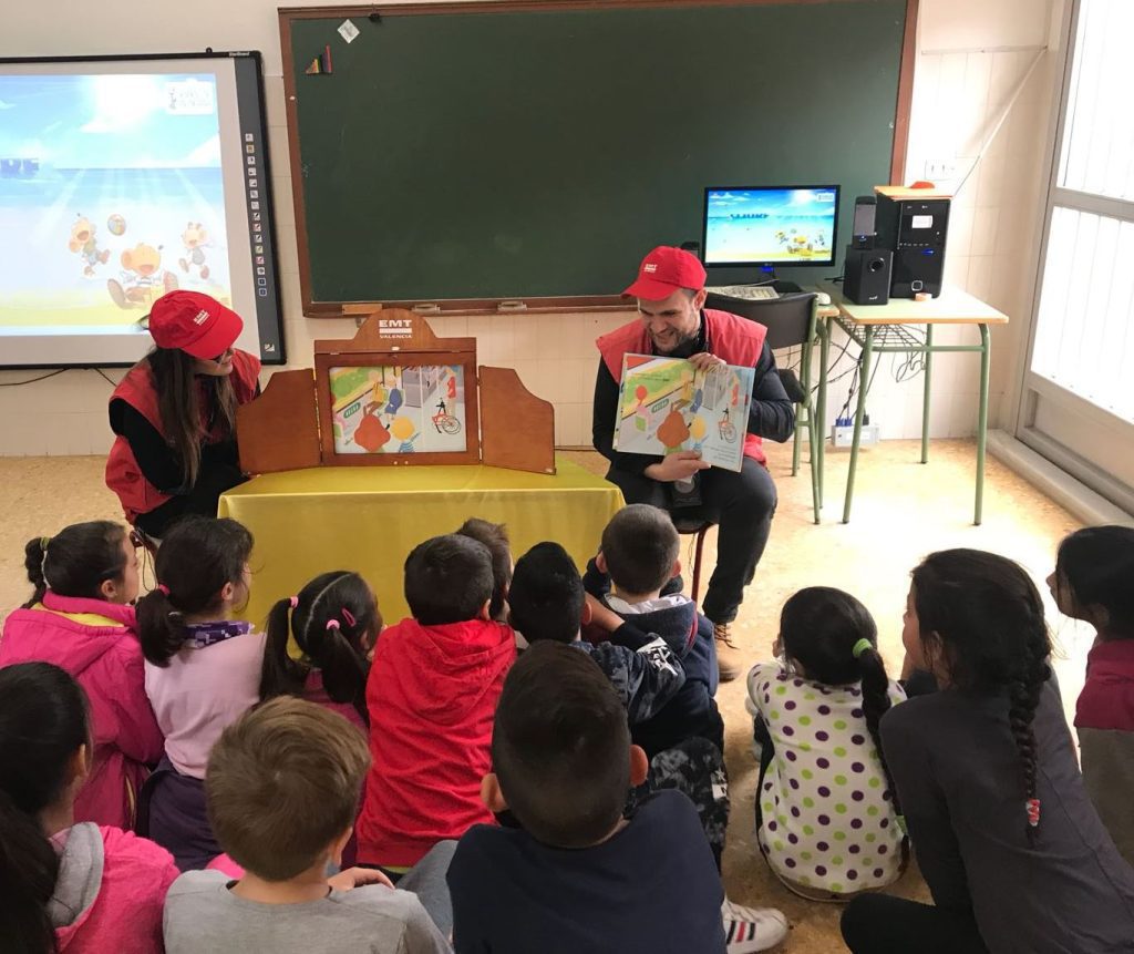 Imagen de dos trabajadores de la EMT dando un taller de movilidad sostenible a través de cuentos,  a alumnos en el aula de un colegio